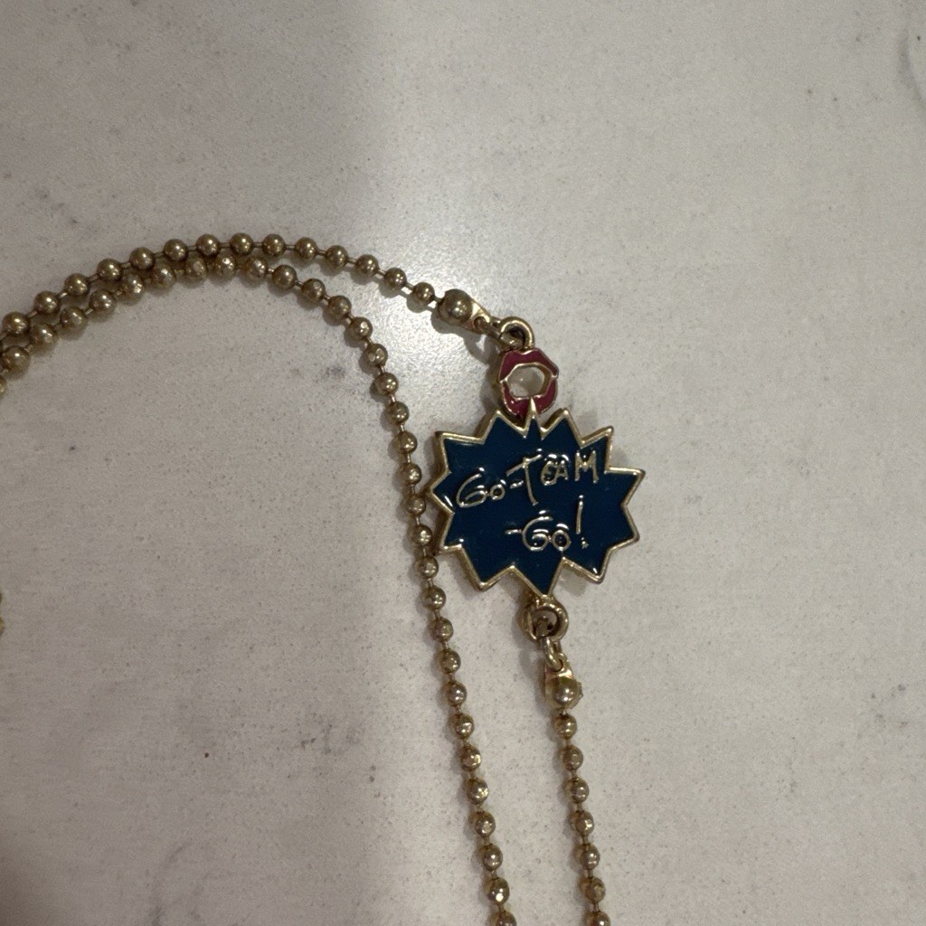 Gold-tone Betsy Johnson whistle necklace with rhinestones, a heart, and a charm.