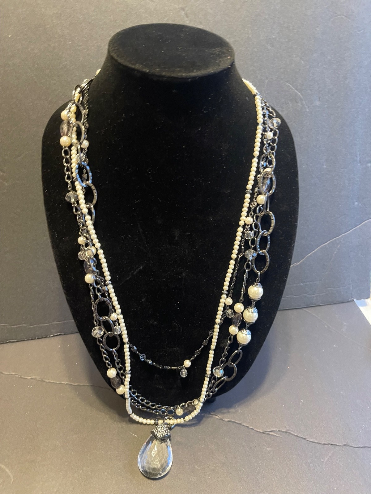Multi-strand layered necklace features gunmetal chains, mixed pearls, clear bead