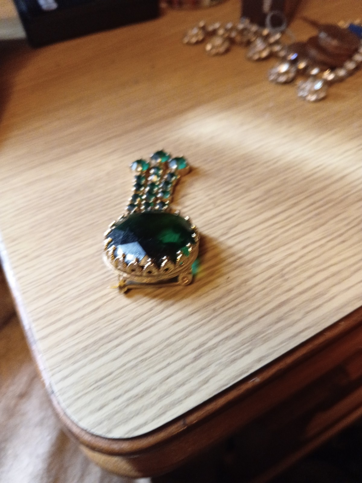 This vintage-style brooch features a large, dark green central rhinestone.