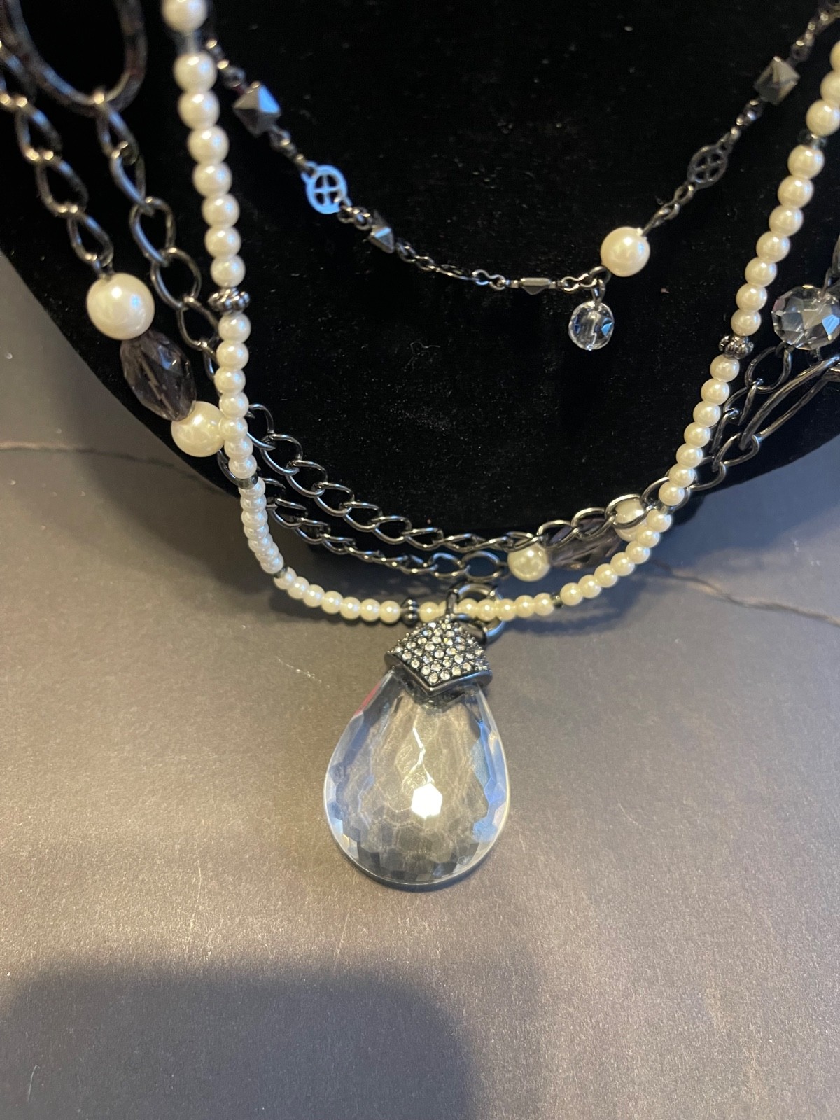 Multi-strand layered necklace features gunmetal chains, mixed pearls, clear bead