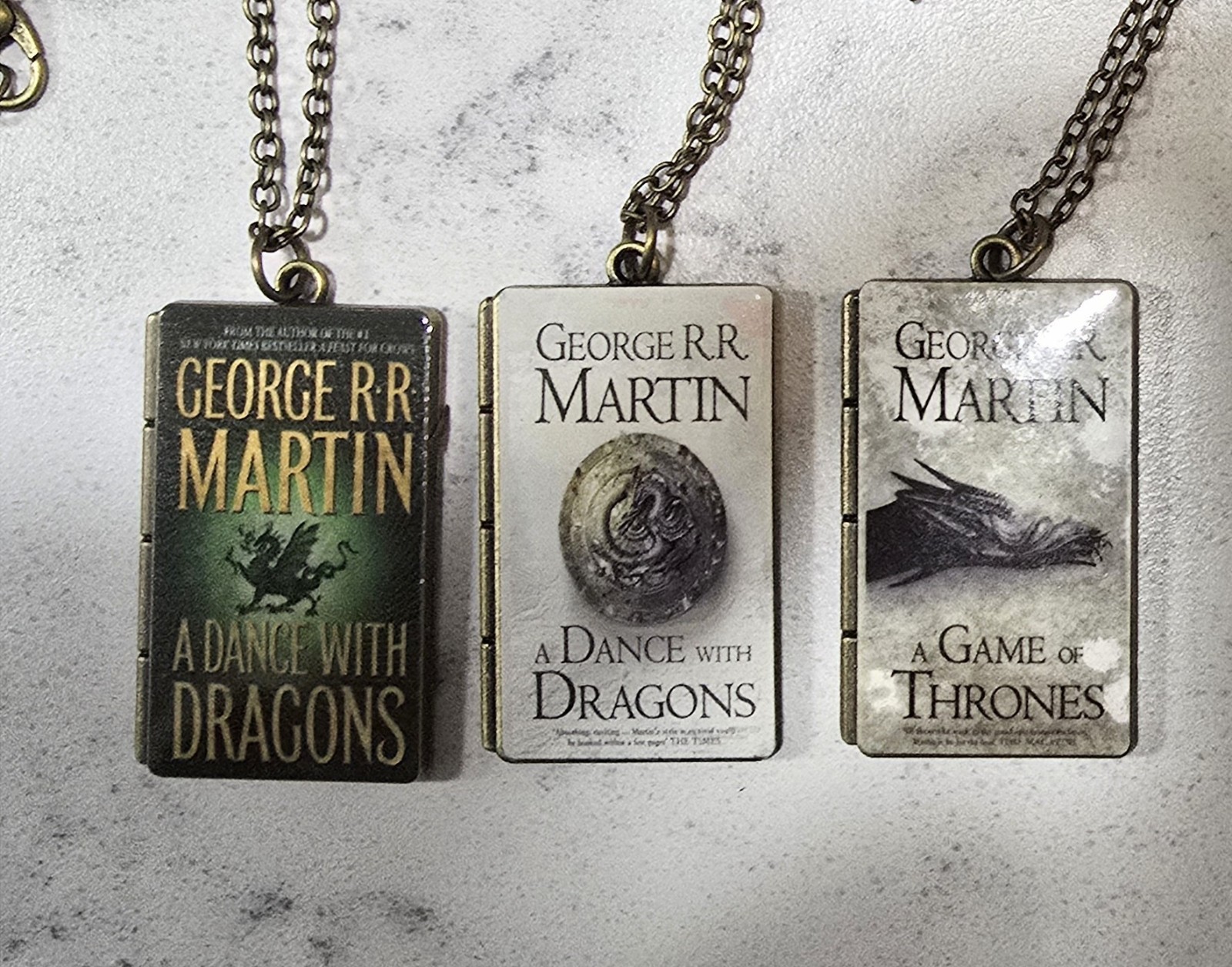 Three George R.R. Martin Book Cover Pendants With Chains – About 1 Inch Each