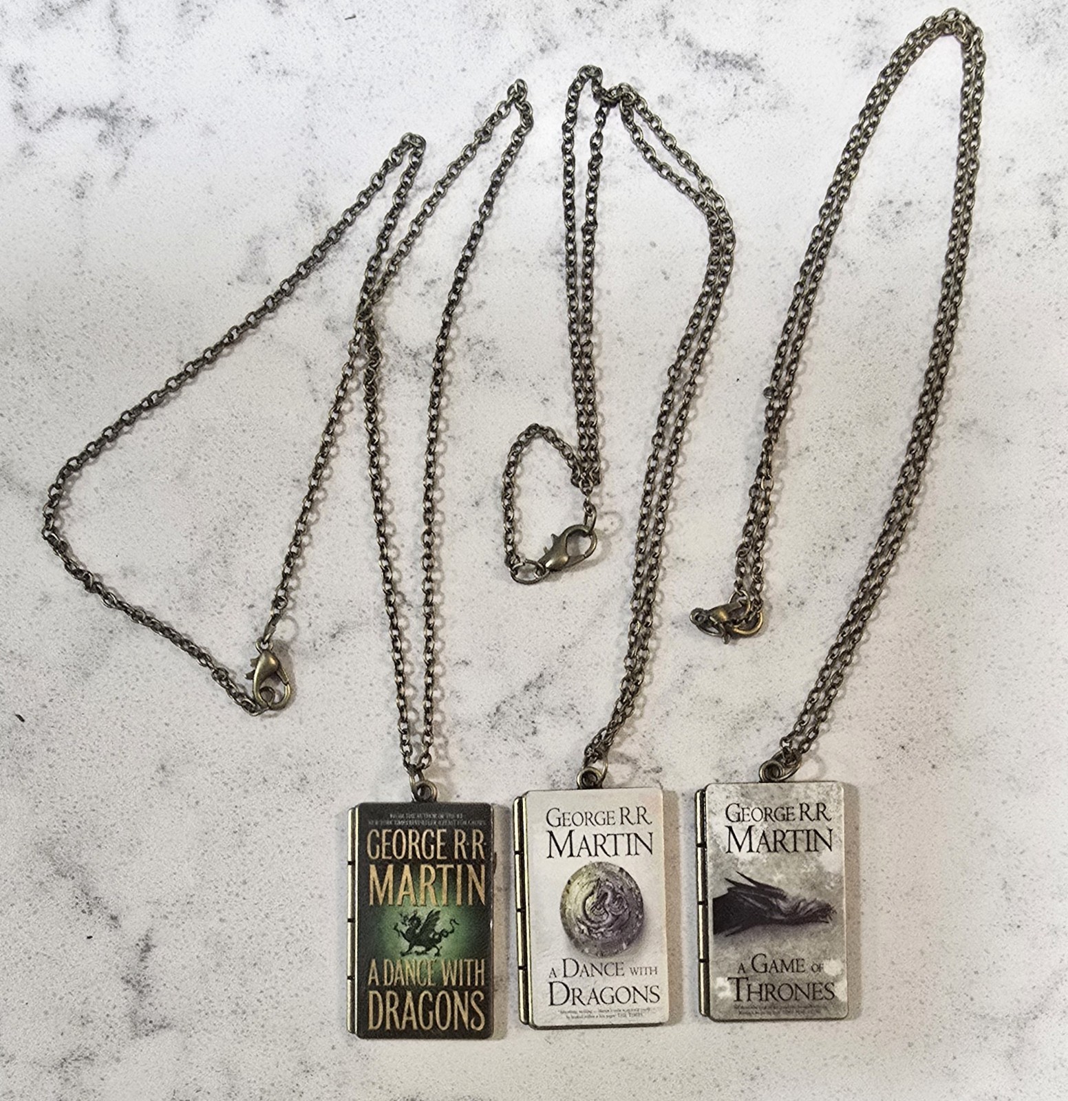 Three George R.R. Martin Book Cover Pendants With Chains – About 1 Inch Each