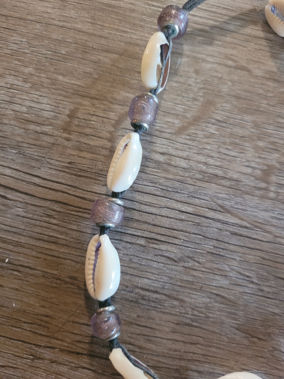 boho-style cowrie shell choker necklace featuring purple beads on a cord.