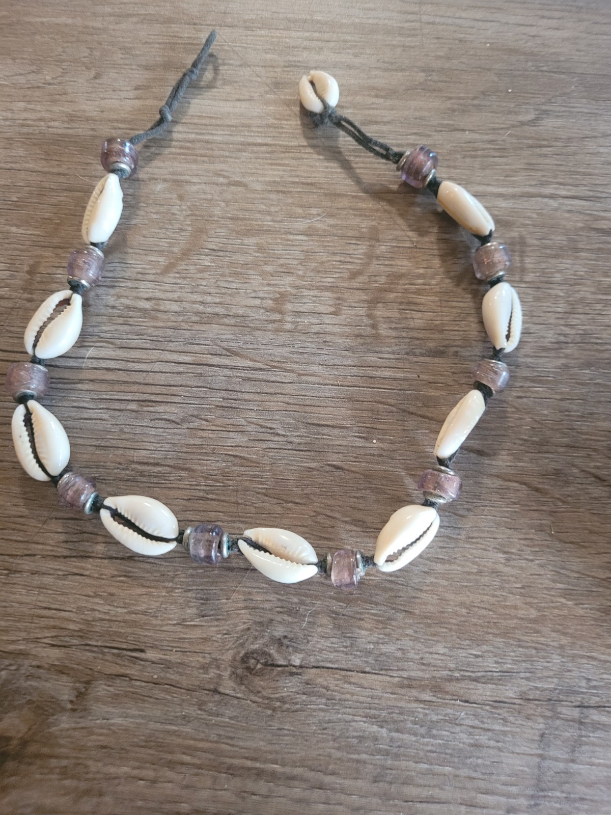 boho-style cowrie shell choker necklace featuring purple beads on a cord.