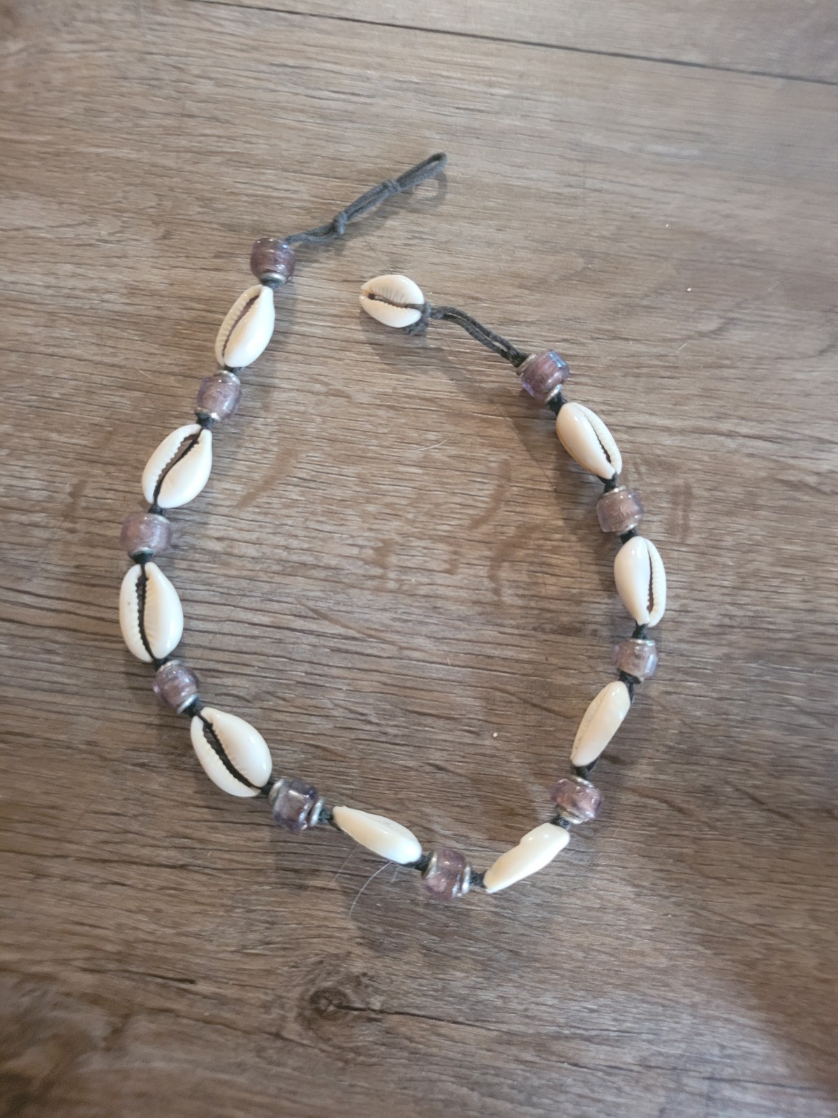 boho-style cowrie shell choker necklace featuring purple beads on a cord.