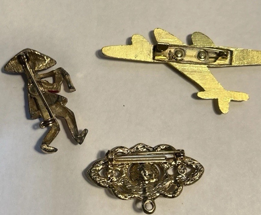 Lot Of 3 Jewelry Pieces Depicting A Rural Farmer, A Floret, Messerschmit plane