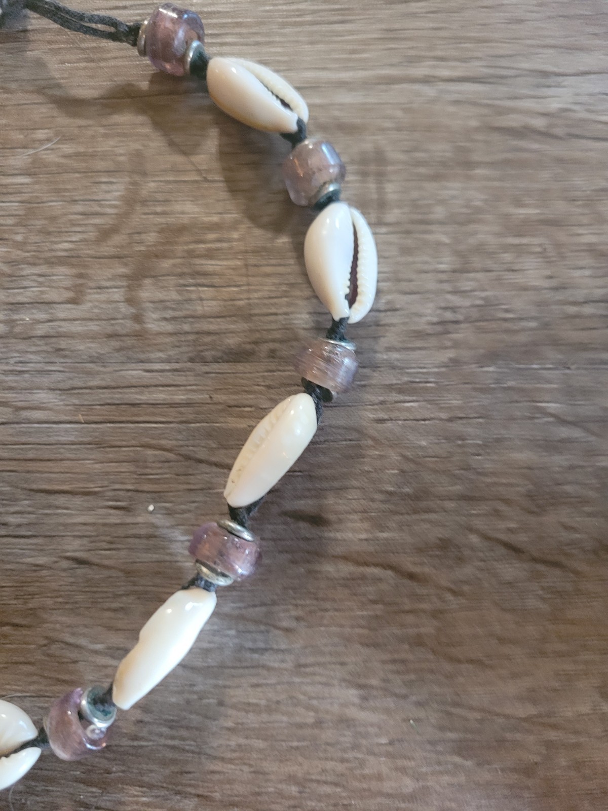 boho-style cowrie shell choker necklace featuring purple beads on a cord.