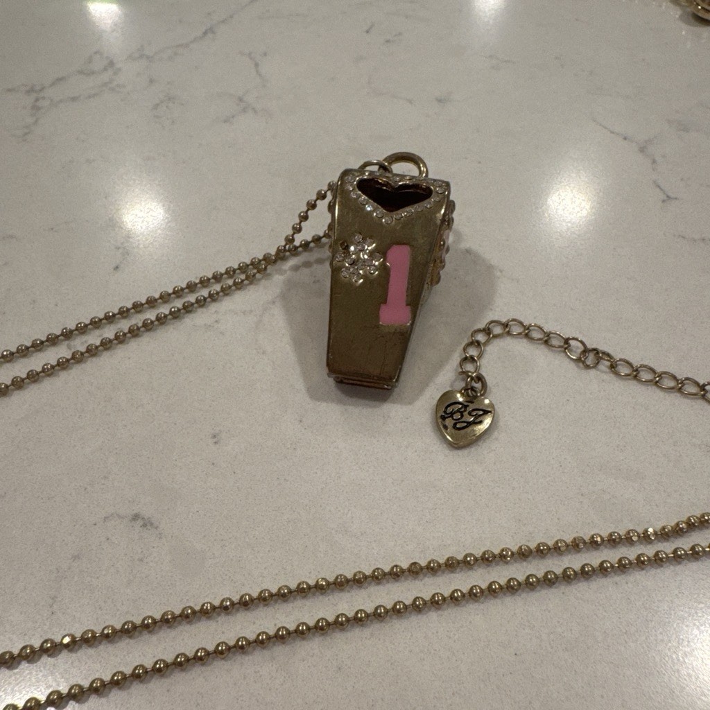 Gold-tone Betsy Johnson whistle necklace with rhinestones, a heart, and a charm.