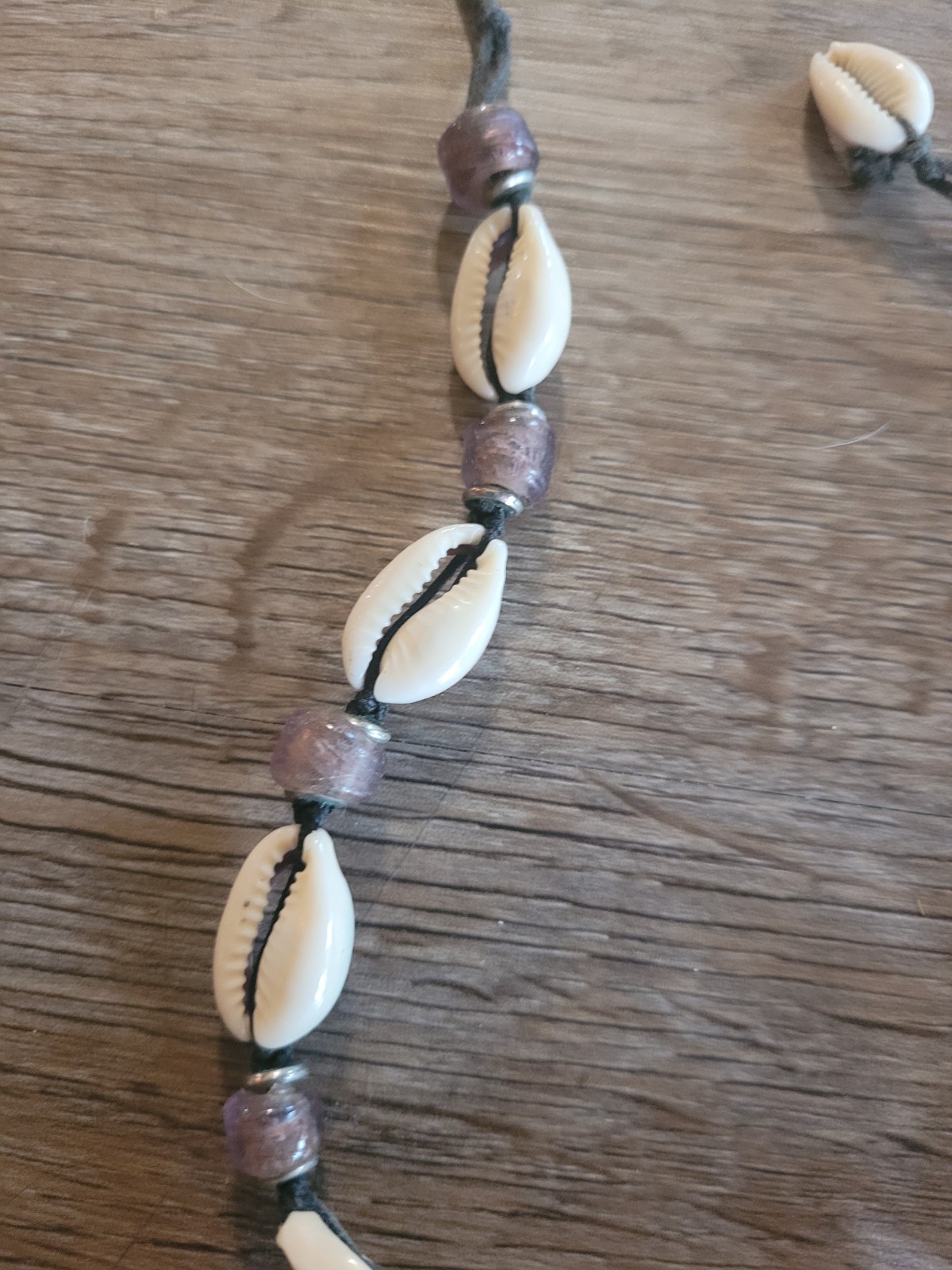 boho-style cowrie shell choker necklace featuring purple beads on a cord.