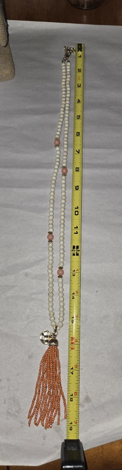 This cream and gold bead necklace features a long orange seed-bead tassel